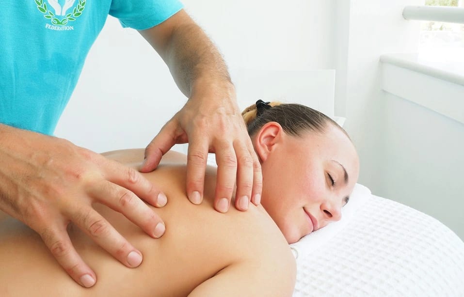 A close-up of both hands working gently across a client's shoulder and upper back.
